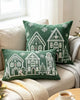 Green Christmas village embroidered pillows on a cream sofa beside a knitted throw