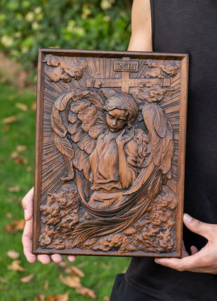Quadratische Holztafel mit geschnitztem Engelrelief, von Händen gehalten, detailreiche Umrandung.