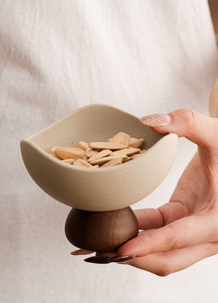 Keramikschale auf Holzsockel, Hand greift Schale mit Nudelsnacks