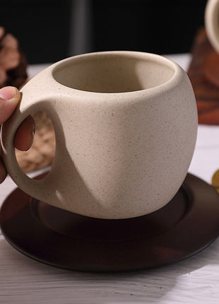 Beige Keramiktasse mit Henkel auf dunklem Holzuntersetzer, Hand hält die Tasse