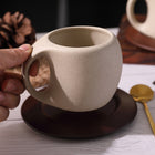 Beige Keramiktasse mit Henkel auf dunklem Holzuntersetzer, Hand hält die Tasse
