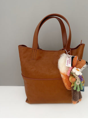 Flower fox wool felt charm hanging from a brown tote bag