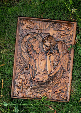 Quadratische Holztafel mit Engelrelief, geschnitzten Flügeln und Kreuz über dem Kopf.