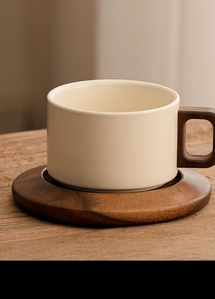 Cremefarbene Keramiktasse mit rechteckigem Holzgriff auf brauner Untertasse