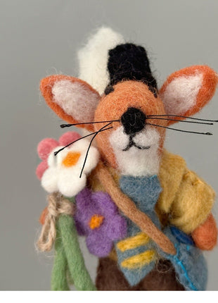 Close-up of orange wool felt fox charm with a bouquet and colorful outfit