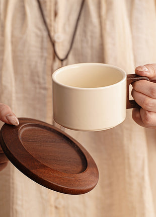 Cremefarbene Keramiktasse mit Holzgriff, Untertasse wird abgehoben