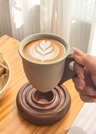 Kaffeetasse aus Keramik mit Holzuntersetzer, befüllt, Hand hält am Henkel