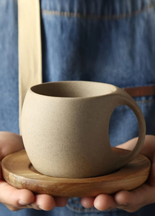 Keramiktasse mit Akazienholz-Tablett, beiger Ton in den Händen gehalten