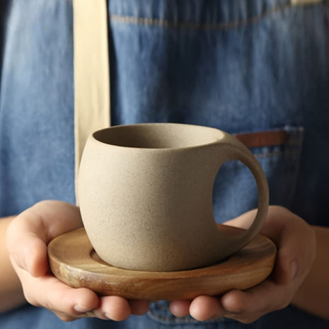 Keramiktasse mit Akazienholz-Tablett, beiger Ton in den Händen gehalten