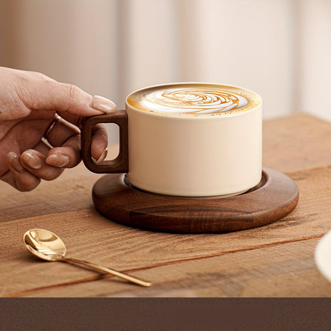 Cremefarbene Keramiktasse auf Untertasse mit Latte-Art, Hand am braunen Holzgriff