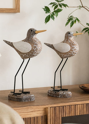 Zwei braun-weiße Holz-Seevögel mit weißem Bauchbereich und Metallbeinen auf Sockeln