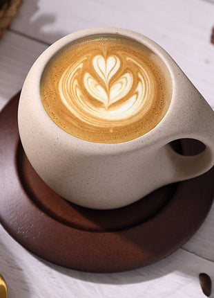 Beige Keramiktasse mit Henkel auf dunklem Holzuntersetzer, Latte-Art im Inneren
