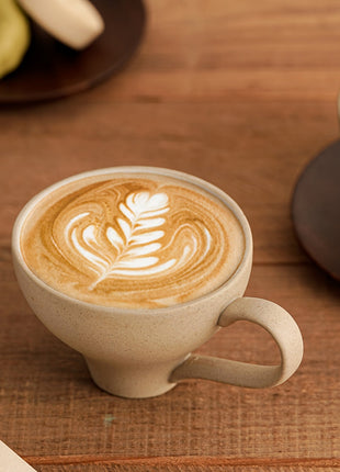 Beigefarbene Keramiktasse mit Latte-Art auf braunem Untersetzer