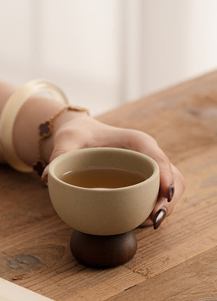 Beige Steingut-Kaffeetasse im Griff, Schale mit dunklem Standfuß auf Holzoberfläche