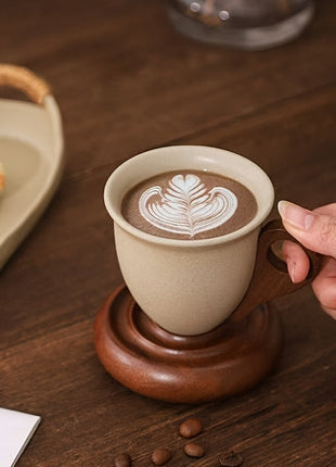 Kaffeetasse aus Keramik mit beigem Henkelbereich und Holzuntersetzer, Latte-Art sichtbar