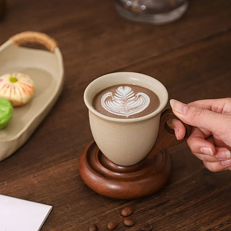 Kaffeetasse aus Keramik mit beigem Henkelbereich und Holzuntersetzer, Latte-Art sichtbar