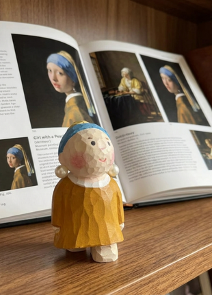 Handgefertigte Holzskulptur: Figur mit blauem Kopftuch, gelbem Kleid und hellem Gesicht.