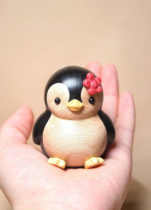 Bemalte Holzfigur: Pinguin mit roter Blume, in einer Hand gehalten