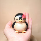 Bemalte Holzfigur: Pinguin mit roter Blume, in einer Hand gehalten