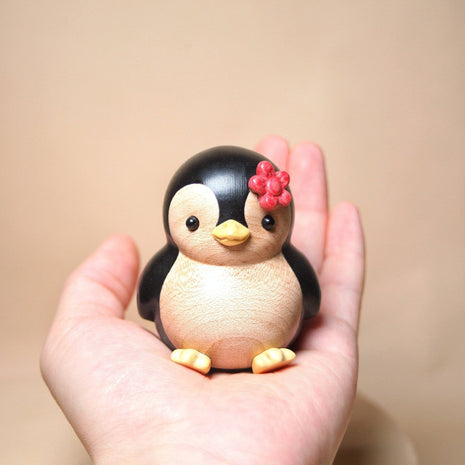 Bemalte Holzfigur: Pinguin mit roter Blume, in einer Hand gehalten