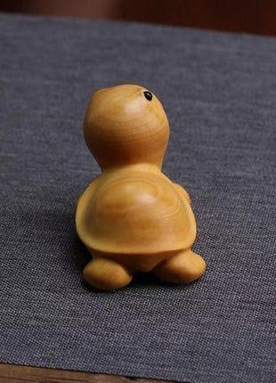 Lächelnde Schildkröten-Holzfigur aus hellgelbem Holz, von der Seite sitzend.