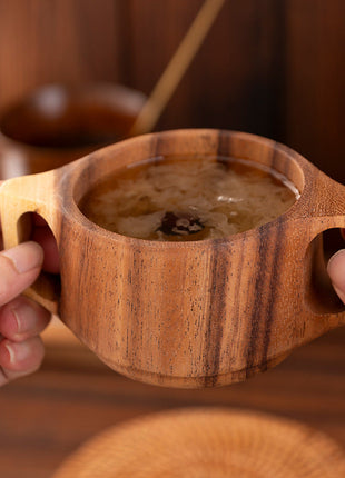 Akazienholz-Tasse mit Doppelgriffen, von Händen gehalten, mit braunem Inhalt