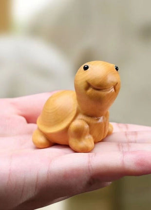 Lächelnde Schildkröten-Holzfigur aus hellgelbem Holz, auf der Handfläche sitzend.