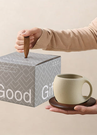 Person reicht hellbeige Steingut-Kaffeetasse mit braunem Holzuntersetzer