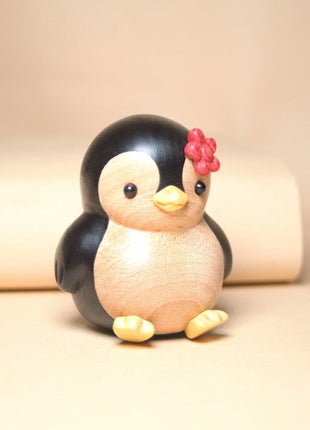 Bemalte Holzfigur: Pinguin mit roter Blume, seitliche Ansicht mit gelben Pfoten