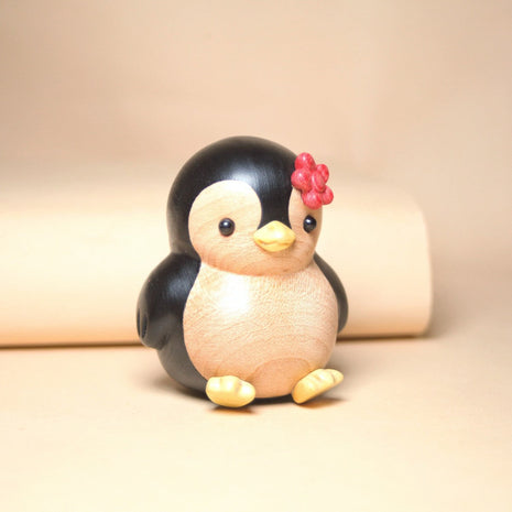 Bemalte Holzfigur: Pinguin mit roter Blume, seitliche Ansicht mit gelben Pfoten