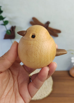 Nahaufnahme: Hand hält Holz-Spatzfigur aus hellem Buchenholz