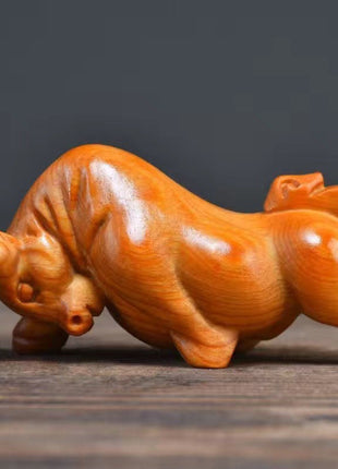 Holzfigur eines Stiers aus Thuja-Holz, liegend, orangebraun, Kopf nach links, Beine ausgestreckt.