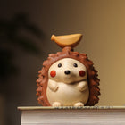 Mini-Igel-Figur frontal mit Holz-Nussaufsatz auf Buchrand, klar ausgerichtet