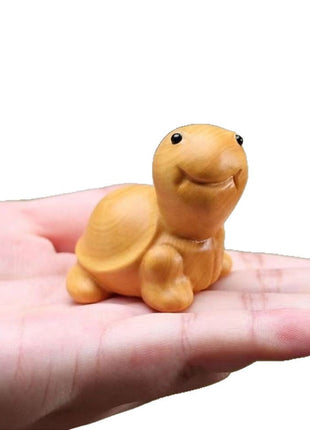 Lächelnde Schildkröten-Holzfigur aus hellgelbem Holz, auf Handfläche liegend.