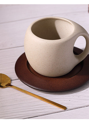 Hellbeige Steingut-Kaffeetasse mit braunem Holzuntersetzer und goldenem Löffel
