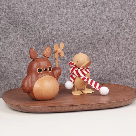 Holzfigur mit Windrad auf Teller-Tablett, neben kleiner Kuscheltier-Figur.