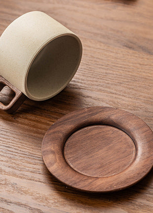 Beige Keramiktasse mit Holzgriff, neben rundem Holzuntersetzer