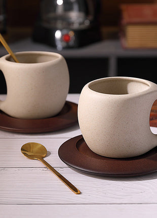 Hellbeige Steingut-Kaffeetasse mit braunem Holzuntersetzer und goldenem Löffel