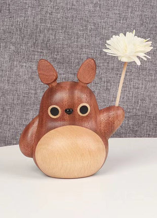 Totoro-Holzfigur mit Windrad und weißer Holzblume auf rundem Kopf als Deko.
