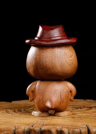 Handgeschnitzte Holzfigur einer Anime-Ente mit braunem Hut, auf rundem Sockel