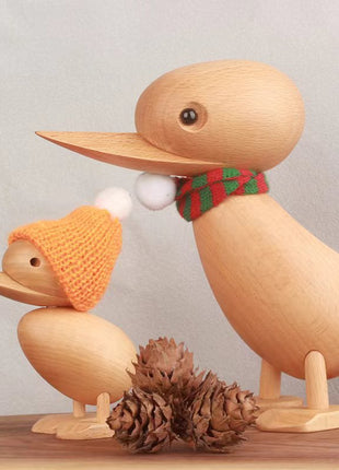 Massivholz-Ente mit grün-rotem Schal, gelber Mütze und weißem Bommel, auf Sockel