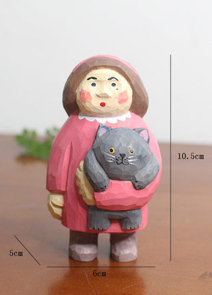 Holzfigur mit rotem Haarschopf, die eine graue Katze trägt