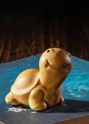Lächelnde Schildkröten-Holzfigur aus hellgelbem Holz, aufrecht geduckt liegend.