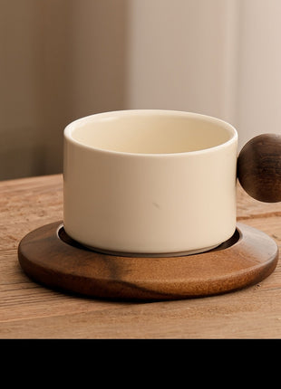 Cremefarbene Keramiktasse mit braunem Holzgriff auf Untertasse, seitlicher Blick