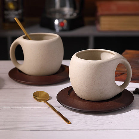 Beige Keramiktasse mit Henkel auf dunklem Holzuntersetzer, goldfarbener Löffel