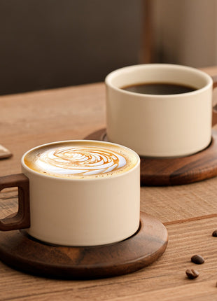 Cremefarbene Keramiktasse mit Untertasse und braunem Griff, Espresso mit Latte-Art.