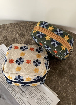 Ivory and olive floral embroidered pouches styled on a magazine