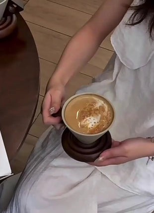 Person hält Trichter-Keramiktasse mit Getränk auf Spiralsockel aus Holz