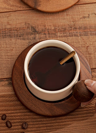 Cremefarbene Keramiktasse mit braunem Holzgriff auf Untertasse, gefüllt mit Kaffee