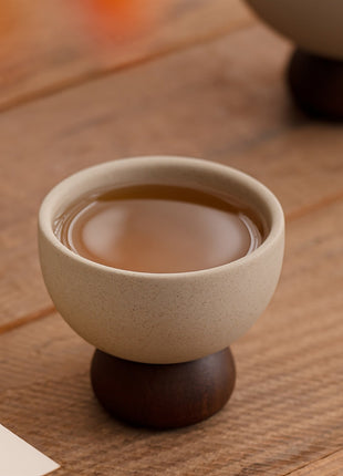 Beiger Kaffeebecher aus Steingut mit dunklem Standfuß, innen mit braunem Getränk